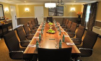 a long wooden table with a centerpiece and empty glasses , set in a conference room with chairs and a television at Oak Island Resort & Conference Centre