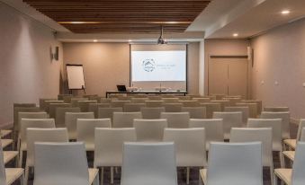a conference room with rows of white chairs and a projector screen at the front at Pedras do Mar Resort & Spa