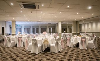 a large banquet hall filled with round tables and chairs , ready for a wedding or other formal event at Holiday Inn Leeds - Garforth