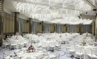 a large , white - themed banquet hall with multiple tables set for dining and a chandelier hanging from the ceiling at Divan Mersin