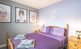 a cozy bedroom with a purple bedspread , two towels neatly folded on the bed , and a lamp hanging from the ceiling at Trenewydd Farm Holiday Cottages