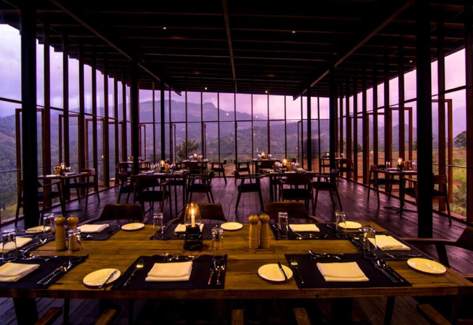 a large , modern restaurant with wooden tables and chairs , set for a formal dinner , has a view of the mountains at Santani Wellness Kandy