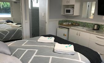 a neatly made bed with a gray and white patterned comforter , two white towels folded on top of it , and a kitchenette area at Ulladulla Motel