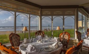 a dining room with a table set for a meal , surrounded by windows that offer a view of the ocean at Sandhouse Hotel