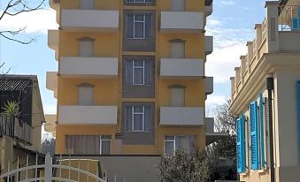 a tall , yellow building with multiple floors and balconies , surrounded by trees and a fence at Hotel Viking