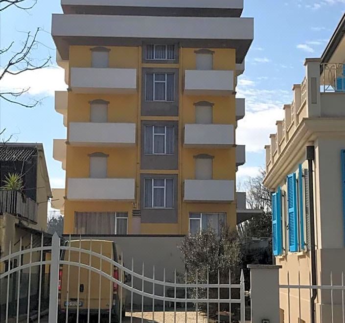 a tall , yellow building with multiple floors and balconies , surrounded by trees and a fence at Hotel Viking