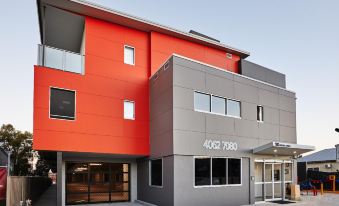 "a modern building with red and gray exterior walls , featuring the name "" 4 0 3 2 7 9 0 "" in white letters" at East Maitland Executive Apartments