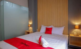 a clean and well - organized hotel room with a white bed , a red comforter , and a lamp on the nightstand at RedDoorz Syariah @ Jalan Sultan Agung Tegal