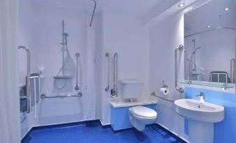 a modern bathroom with white walls , blue flooring , and various amenities such as a shower , toilet , sink , and mirror at Travelodge Nottingham Trowell M1