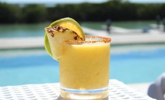 a glass of pineapple juice on a white table , with a slice of pineapple and a wedge of lime garnish at Villas Grand Marina Kinuh