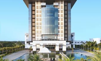 a large building with a tall glass and metal structure is surrounded by palm trees at Le Méridien Coimbatore