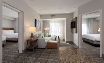 a modern hotel room with a white couch , two lamps , and a tv , along with a desk and a bed at Staybridge Suites Buffalo
