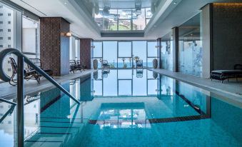 a large indoor swimming pool with a clear blue water and surrounding facilities , including sun umbrellas and lounge chairs at David Tower Hotel Netanya by Prima Hotels - 16 Plus
