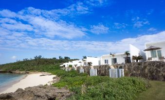 a beach scene with a row of white buildings on the shore , surrounded by trees at Crystal Villa Miyakojima Sunayama Beach
