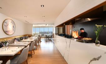 a modern restaurant with white marble tables and chairs , a chef working at the counter , and large windows at Oakwood Apartments PIK Jakarta
