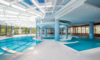 a large indoor swimming pool with a glass roof and blue walls , surrounded by white walls at Mitsis Galini