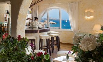 a woman sitting at a bar in a room with a view of the ocean at Club Hotel Baja Sardinia