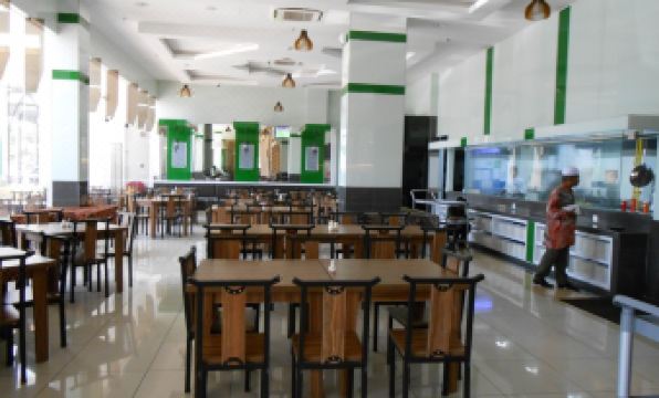 a large dining room with wooden tables and chairs , a fish tank in the background , and people standing at the counter at HIG Hotel & Convention