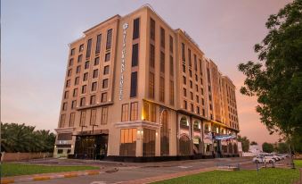 a large hotel building situated on the side of a street , with the sun setting in the background at Ayla Grand Hotel Al Ain