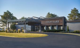 a modern hotel building with a large sign above the entrance , surrounded by trees and grass at Courtyard Chicago Wood Dale / Itasca