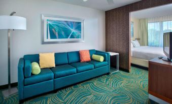 a blue couch with colorful pillows is in a room with a green carpet and a framed picture on the wall at SpringHill Suites Philadelphia Willow Grove