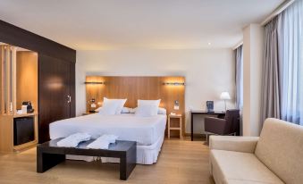 a modern hotel room with a large bed , white bedding , and wooden furniture , along with a living room area at Occidental Hotel Cadiz