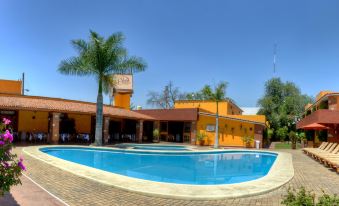 a large swimming pool surrounded by a brick building , with palm trees in the background at Hotel Hacienda