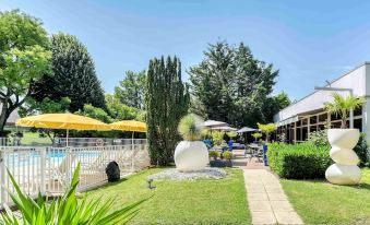 a well - maintained backyard with a pool , umbrellas , and a fountain , surrounded by lush greenery and trees at Novotel Paris Nord Expo Aulnay