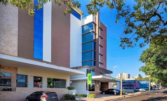 a modern building with a blue and white facade is situated on a street corner , surrounded by cars and trees at Ibis Styles Piracicaba