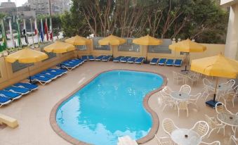 a large outdoor pool surrounded by lounge chairs and umbrellas , with trees in the background at Aracan Pyramids Hotel