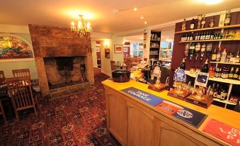 a cozy bar with wooden furniture , a fireplace , and various bottles of alcohol on display at Three Wheat Heads