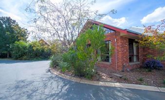 a brick house with a red roof and large windows is surrounded by trees on a sunny day at Perricoota Vines Retreat