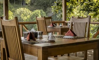 a wooden dining table set with chairs and a cup of coffee on a balcony overlooking a lush green landscape at Janji Laut Resort