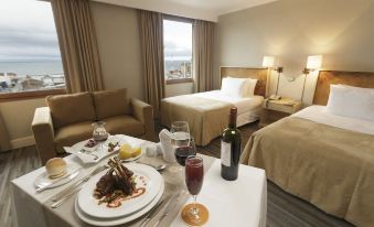 a hotel room with two beds , a dining table with wine glasses , and a bottle of wine at Hotel Cabo de Hornos