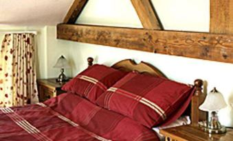 a cozy bedroom with a wooden headboard , red bedspread , and white curtains , lit by small lamps on the ceiling at Hillbrow Farm B&B
