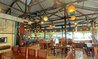 a large , open dining room with wooden tables and chairs , hanging light fixtures , and a central area where people are seated at Rock and Wreck Dive Resort