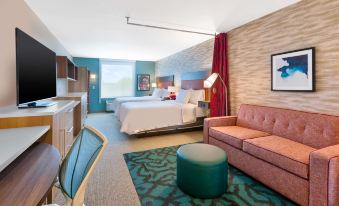 a hotel room with a pink couch , bed , and kitchenette , along with other furniture and decorations at Home2 Suites by Hilton Battle Creek