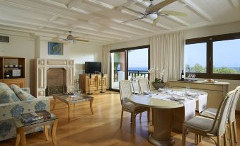 a spacious living room with hardwood floors , a large flat - screen tv mounted on the wall , and a dining table in the corner at Aldemar Knossos Royal