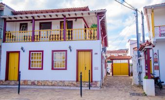 a white building with yellow doors and balconies , situated on a cobblestone street under a blue sky at Pousada Tesouro de MInas