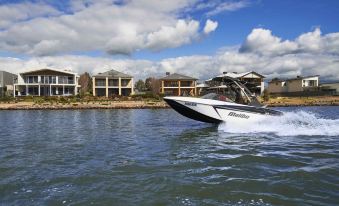 a black and white speedboat is speeding across a body of water near a row of houses at The Sebel Yarrawonga Silverwoods
