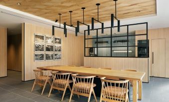 a modern dining room with wooden tables and chairs , a long table surrounded by windows , and black pendant lights hanging from the ceiling at Fairfield by Marriott Mie Kumano Kodo Mihama