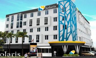 a modern hotel building with a large logo on the side , surrounded by palm trees at Solaris Hotel Malang