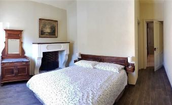 a neatly made bed with a white and floral patterned comforter is situated next to a fireplace at La Fornace