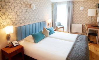 a large bed with blue headboard and white sheets is in a room with gray patterned walls at Fosshotel Eastfjords
