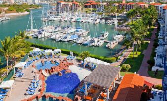 a marina with numerous boats docked , surrounded by buildings and a pool area with lounge chairs at El Cid Marina Beach Hotel
