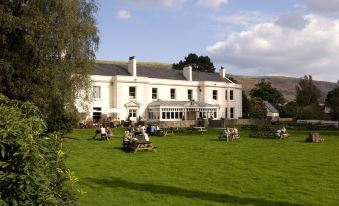 a large white building surrounded by green grass and trees , with people sitting on benches in the lawn at Premier Inn Merthyr Tydfil