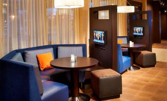 a hotel lobby with blue couches , chairs , and a television mounted on the wall , creating a comfortable seating area at Courtyard Toledo Airport Holland