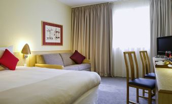 a hotel room with a comfortable bed , a couch , a tv , and a dining table at Novotel Manchester West