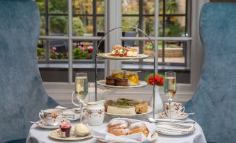 a three - tiered cake stand filled with a variety of desserts , including cakes , cookies , and cupcakes , placed on a dining table at The Holt Hotel