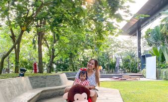 a young girl is sitting on a teddy bear in a park , smiling and enjoying her time at Mercure Tangerang BSD City